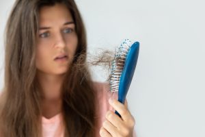 mulher com calvicie, ela esta assustada olhando a escova cheia de cabelo